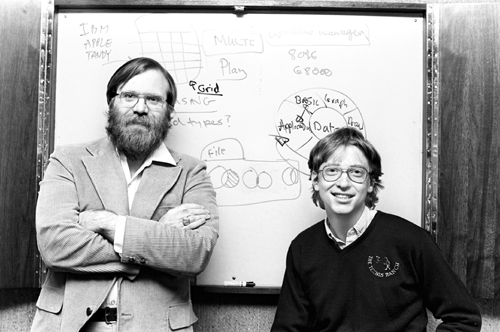 Young Bill Gates and Paul Allen working on a computer in a cluttered garage during the early days of Microsoft in the 1970s.